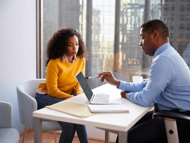 Black Man Manager at desk with laptop open consulting with younger black woman